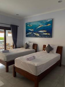 a bedroom with two beds and a painting on the wall at Holiday Guest House in Amed