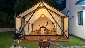 a tent with a grill and a fire in a yard at Gyeongju Gamseong The Glamping Pool Villa in Gyeongju