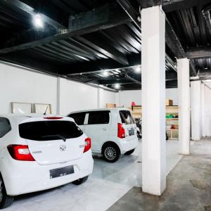 two white cars parked in a parking lot at RedDoorz at Omah Joyo Solo Inn in Solo