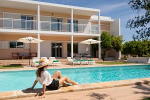 a woman sitting next to a swimming pool in front of a house at New! Villa Margarita - Ibiza in Santa Eularia des Riu