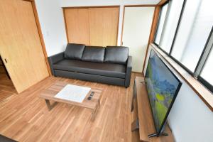 Una sala de estar con un sofá negro y un televisor. en Tomoko's旅館, en Izunokuni