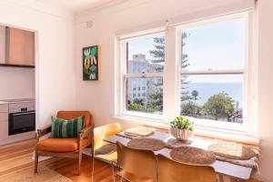 a dining room with a table and chairs and two windows at Ocean Views at The Holkham Fairy Bower in Sydney