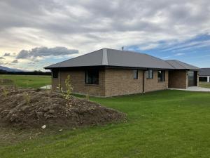 a brick house with a black roof in a field at 3-Bedroom Retreat in Mount Somers in Mount Somers