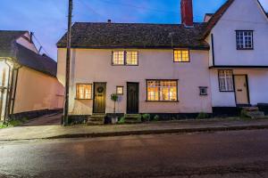 ein weißes Haus mit beleuchteten Fenstern auf einer Straße in der Unterkunft Taper House - Cosy Medieval Cottage in Kersey