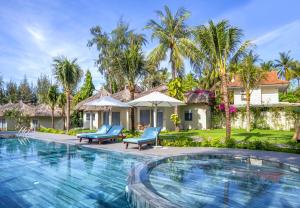 a swimming pool in front of a house with palm trees at Coco Cottage Beachfront Resort in Mui Ne