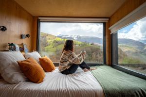 a woman sitting on a bed looking out a window at Parcel Tiny House Bele Ame au coeur des Pyrénées in Germ