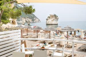 a beach with tables and umbrellas and the ocean at AH Premium Baia dei Faraglioni in Mattinata