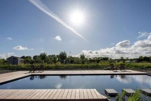 a swimming pool with benches and the sun in the sky at Het Kleine Huis at Buitenplaats Zeeuwse Liefde in Westkapelle