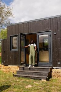 une femme debout à l'entrée d'une petite maison dans l'établissement Parcel Tiny House Brosse 1, pleine nature proche de Sancerre, à La Celle-sous-Gouzon