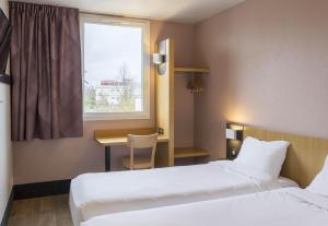a hotel room with two beds and a desk and a window at B&B HOTEL Auxerre Monéteau in Monéteau +64 photos