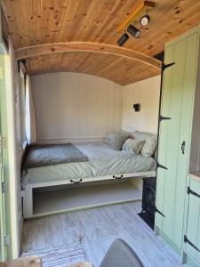 a bed in a tiny house with a wooden ceiling at Clissmann Farm Shepherds Hut in Rathdrum