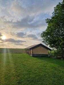 欣德洛彭Glamping Safaritent 4 persoons的田野中的一栋建筑，有树和日落 更多5张照片