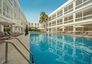 a woman walking by a swimming pool next to a building at RH Silene Hotel & Spa 4 Sup in Castellón de la Plana