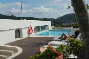 una mujer sentada en una silla junto a una piscina en Fantasea Kamala Beach 1 BR 411, en Kamala Beach