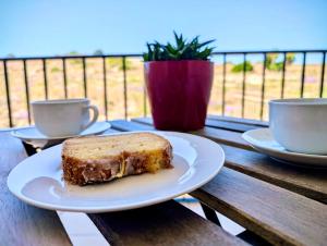 a piece of cake on a plate on a table with two cups at Sunset Haven Manikata - Walking distance to Golden Bay in Manikata