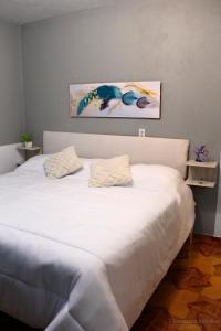 ein Schlafzimmer mit einem weißen Bett und einem Gemälde an der Wand in der Unterkunft Cozy family apartment, kitchen in Mineral del Monte