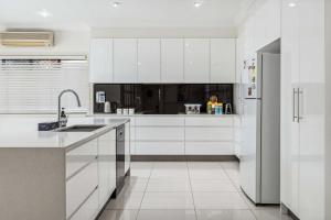 a white kitchen with white cabinets and a refrigerator at CASSA WELLINGTON POINT - Spacious 4BR Home w Pool in Wellington Point