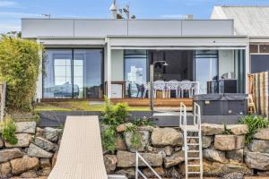 a house with a stone wall and a ladder at Lake Front - Outdoor Hot tub in Merimbula