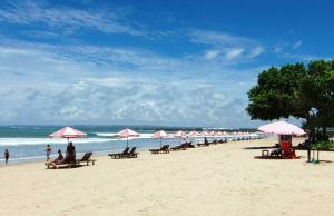 a beach with umbrellas and people sitting on the beach at SH Hotel Kuta- 20 Second to the Beach by Micky Studio in Legian
