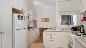 Una cocina con gabinetes blancos y un refrigerador blanco. en Crabapple Southside Mountain Cottage Pet Friendly, en Wentworth Falls
