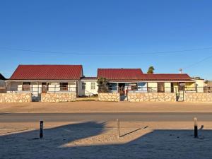 a building with red roofs and a road in front at Grazia Cottages in Port Nolloth