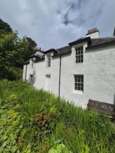 un bâtiment blanc sur une colline avec de l'herbe et des fleurs dans l'établissement Mackinnon Cottage - 3 bedroom Cottage, à Broadford