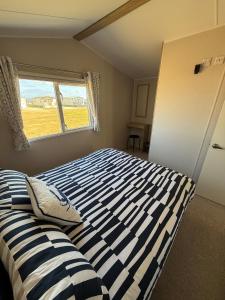 a bedroom with a bed with a striped comforter and a window at 36 Lighthouse View in Lossiemouth