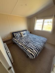 a bedroom with a bed with a striped comforter and a window at 36 Lighthouse View in Lossiemouth