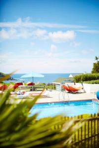 ein Swimmingpool mit Liegen und Sonnenschirmen und das Meer in der Unterkunft St Moritz Hotel Houses in Polzeath