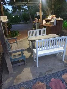 two white benches and a table and a chair at บ้านพักคุณยายเขียว in Ban Thung Kham