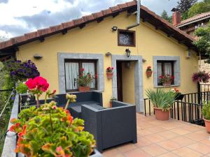 una pequeña casa amarilla con flores delante en El Hayedo de Argovejo, en Argovejo