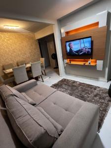 a living room with a couch and a tv on a wall at Apartamento em Frente ao Shopping Itaguaçu in São José