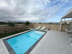 una piscina con 2 sillas y una pared de piedra en Villa Ginevra, en Otranto