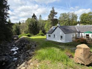 a white house with a river in front of it at Drumlinn Cottage in Bridge of Cally