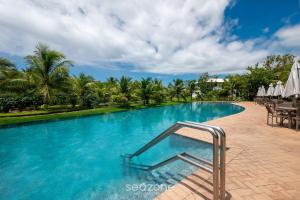 a swimming pool with blue water and palm trees at Apto em Cond. c/piscina em Praia do Forte CVAF0220 in Praia do Forte