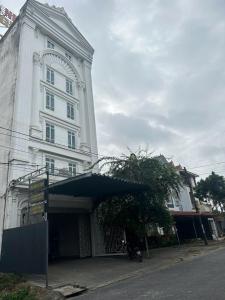 a tall white building with a building with a tree in front at Nhà Nghỉ Gia Anh in An Dương