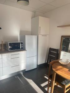 a kitchen with white cabinets and a table and a microwave at Chez Ambre et Lulu - Appartement centre ville avec piscine in Millau
