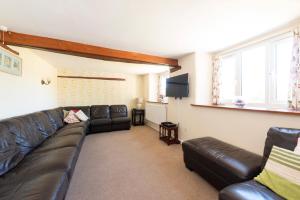 a living room with a leather couch and a flat screen tv at Tanglewood Cottage - Lancombes House in Powerstock