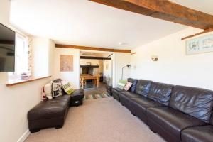 a living room with a black leather couch at Tanglewood Cottage - Lancombes House in Powerstock