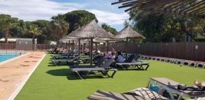 a group of lawn chairs and umbrellas next to a pool at camping la palmeraie chez caro et gui in Torreilles