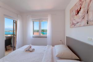 a white bedroom with a bed and a window at Apartments Omanović in Čižići