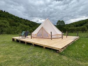 een tent en twee stoelen op een houten terras bij Glamping - Casuta de pe Fiad in Romuli