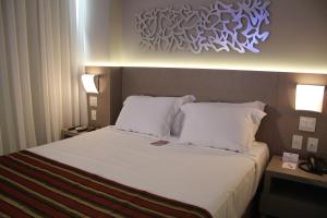 um quarto de hotel com uma cama com lençóis brancos e almofadas em Hotel Beaga Convention Expominas by MHB em Belo Horizonte