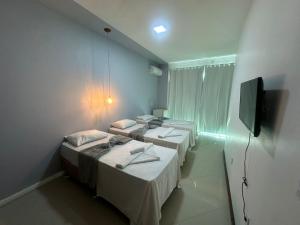 a room with three beds and a flat screen tv at Pousada Aroeira in Arraial do Cabo