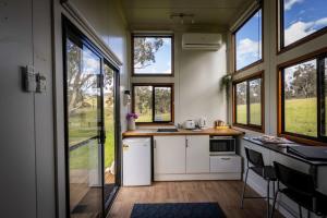 una cucina con armadietti bianchi, finestre e bancone di Sithuri Tiny House by Tiny Away a Windeyer