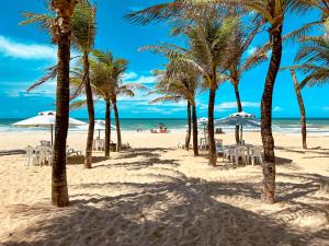 a beach with chairs and palm trees and the ocean at Luxo e Conforto à Beira-Mar com acesso direto para a praia no Porto das Dunas com 3 suítes, ideal para Famílias Exigentes in Aquiraz