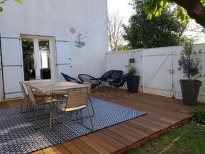 eine Holzterrasse mit einem Tisch und Stühlen darauf in der Unterkunft Maison spacieuse pour 8 au Bois-Plage-en-Ré avec jardin - FR-1-835-13 in Le Bois-Plage-en-Ré