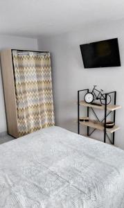 a bedroom with a white bed and a television at La petite ruette in Le Molay-Littry