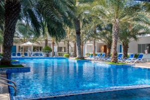 a pool with palm trees and lounge chairs at Fujairah Hotel & Resort in Fujairah