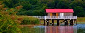 a house with a red roof on a dock in the water at Maison calme in Bazouges-sous-Hédé